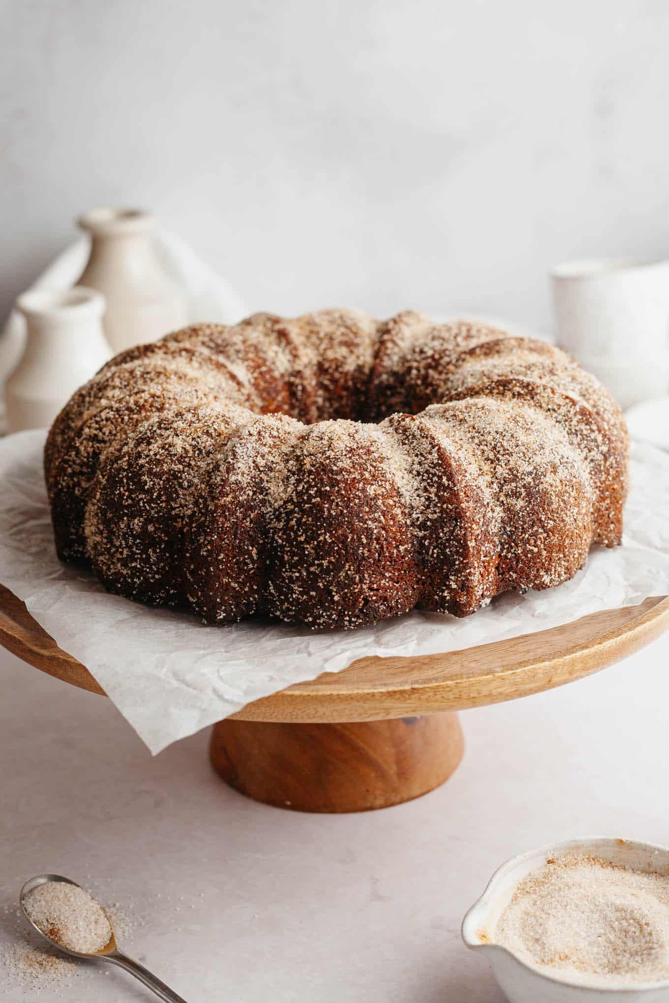 A cinnamon sugar-coated apple donut cake on a wooden cake stand. 