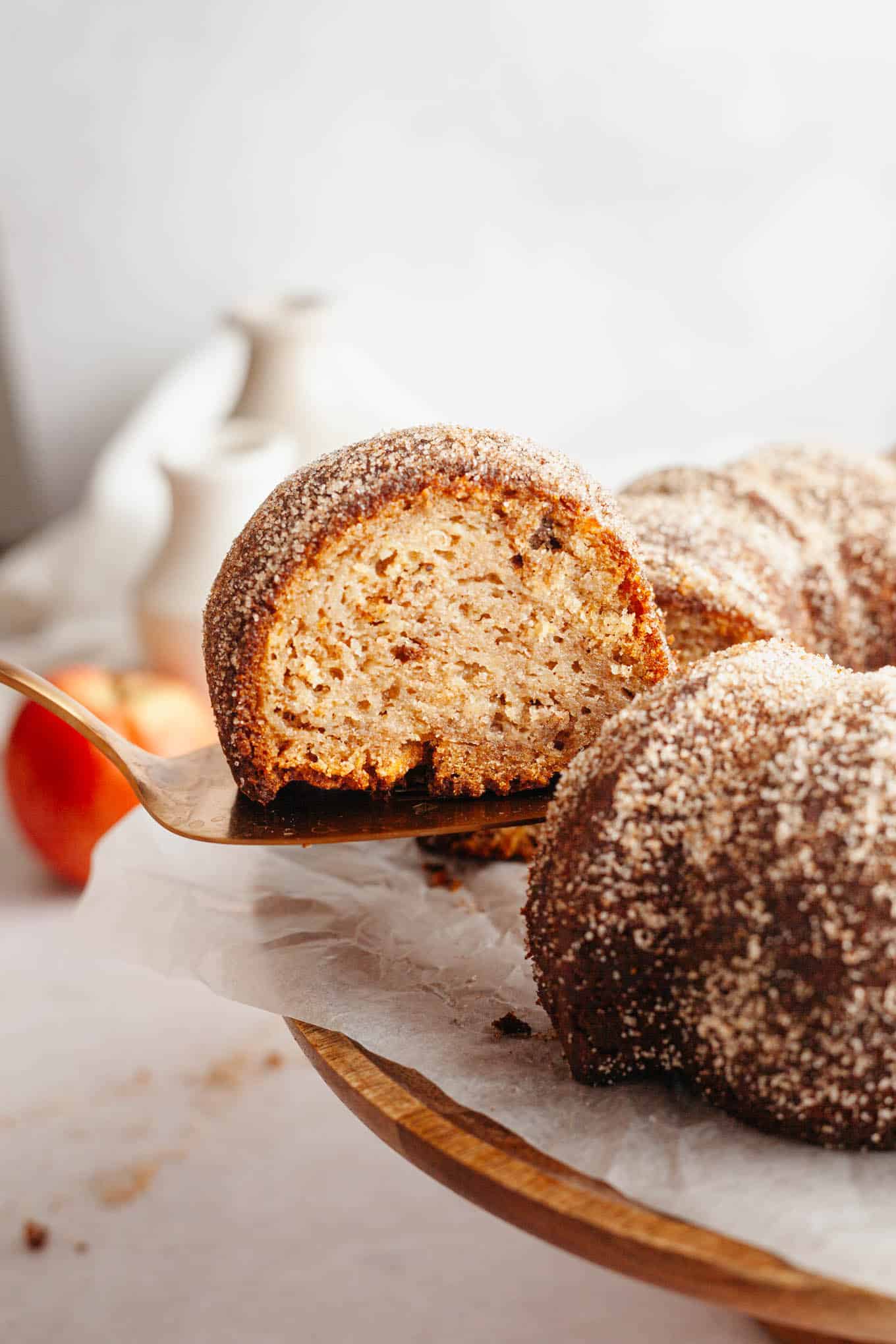 A slice of apple cider donut cake being lifted from a cake stand. 