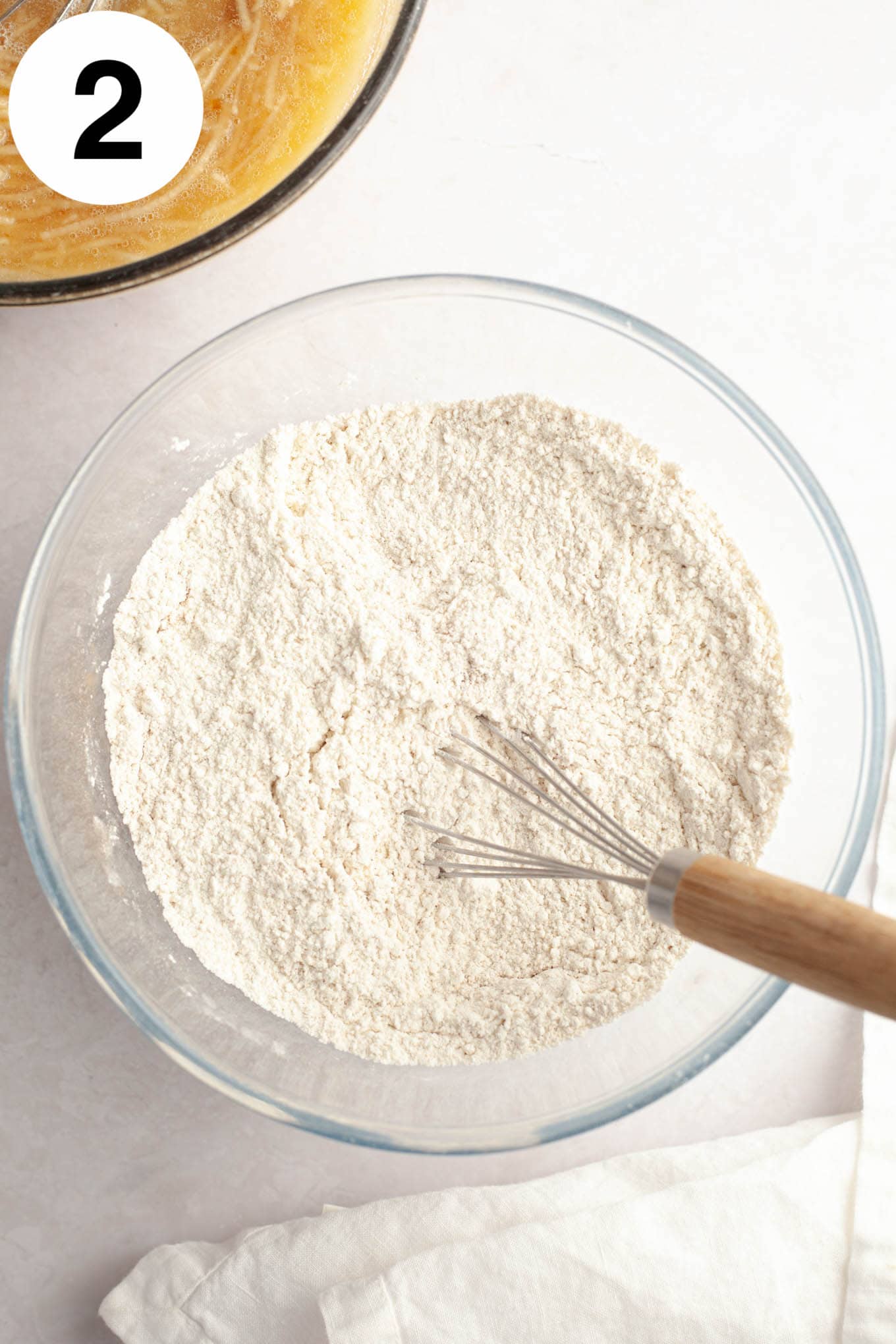An overhead view of a flour and spice mixture, in a glass mixing bowl with a whisk. 