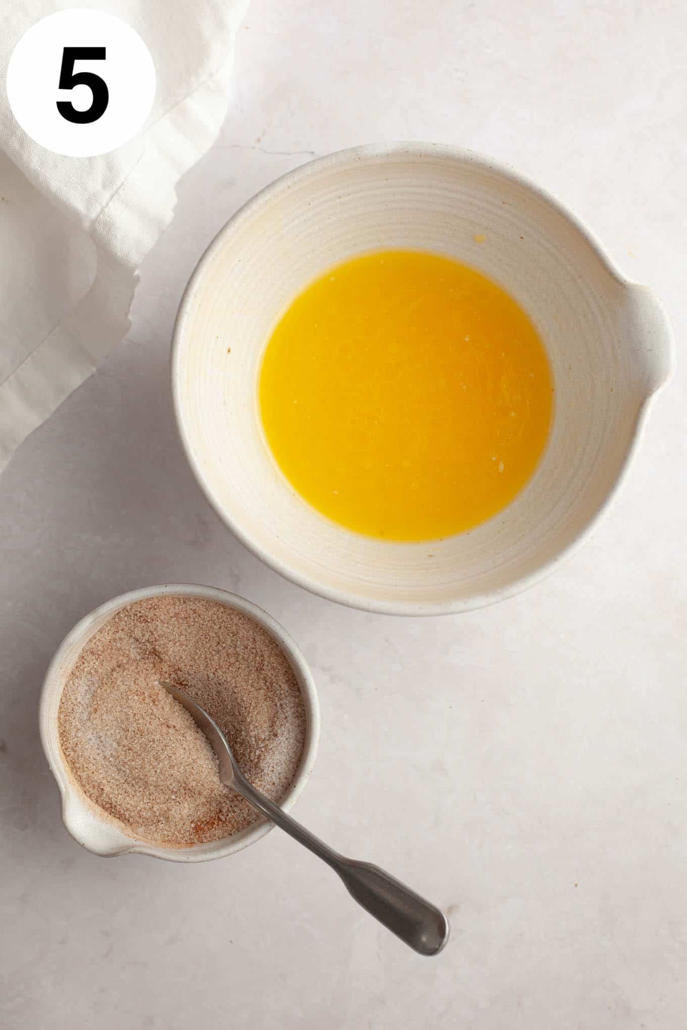 An overhead view of a melted butter mixture and cinnamon sugar, in two bowls. 