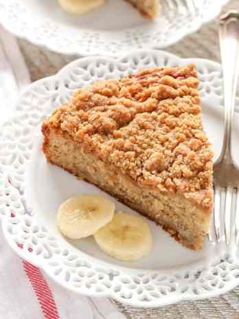 A slice of banana cake on a white plate. A fork and banana slices are also on the plate.