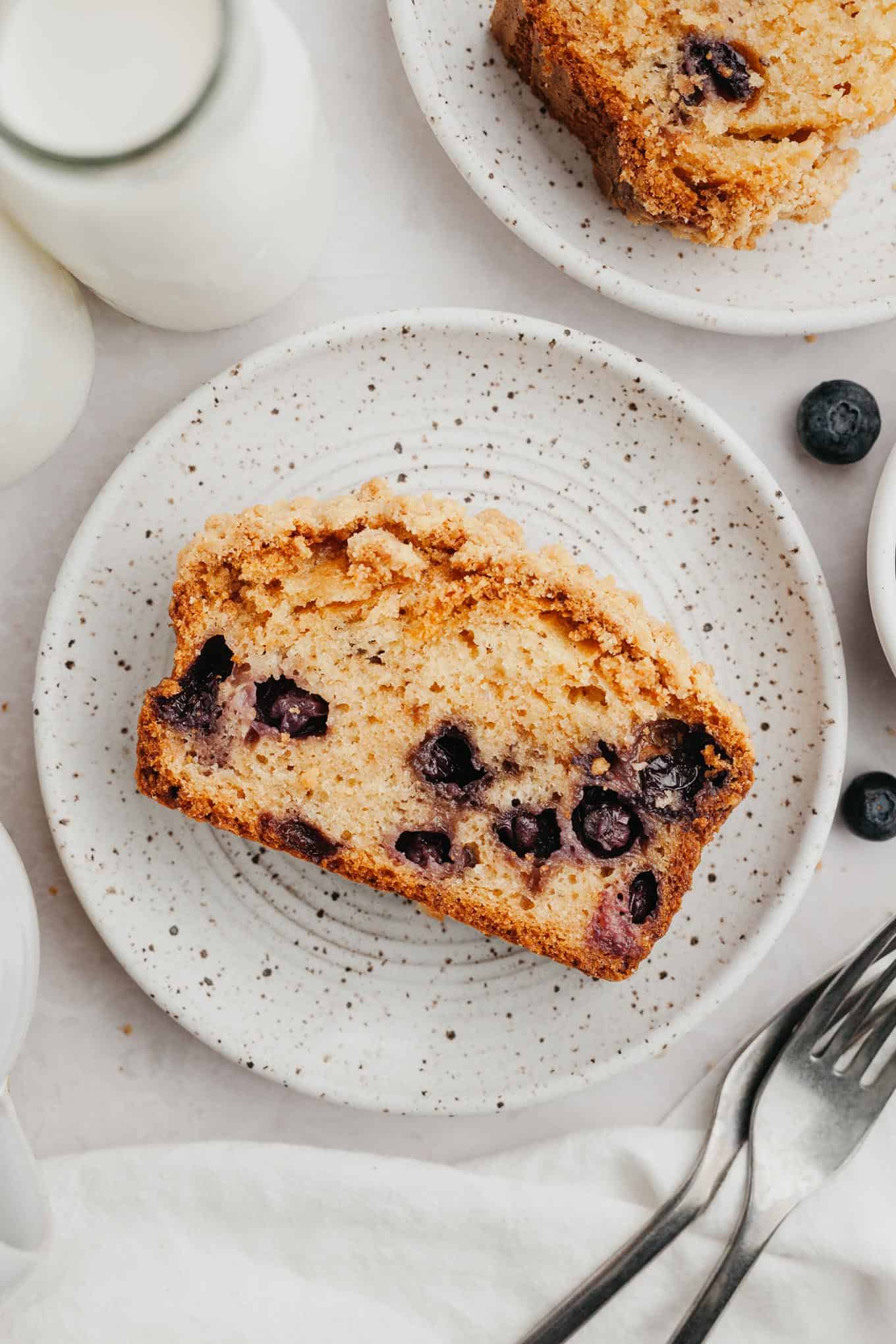 An overhead view of a slice of blueberry streusel bread on a speckled white plate. 