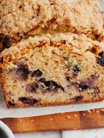 A loaf of blueberry bread that's been sliced on a wooden cutting board.