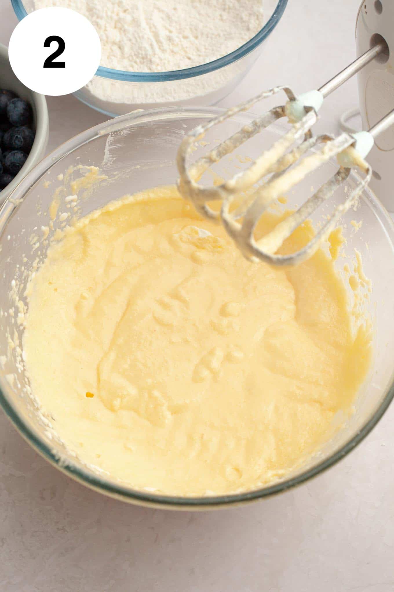 An overhead view of a butter mixture in a glass mixing bowl, with electric beaters. 
