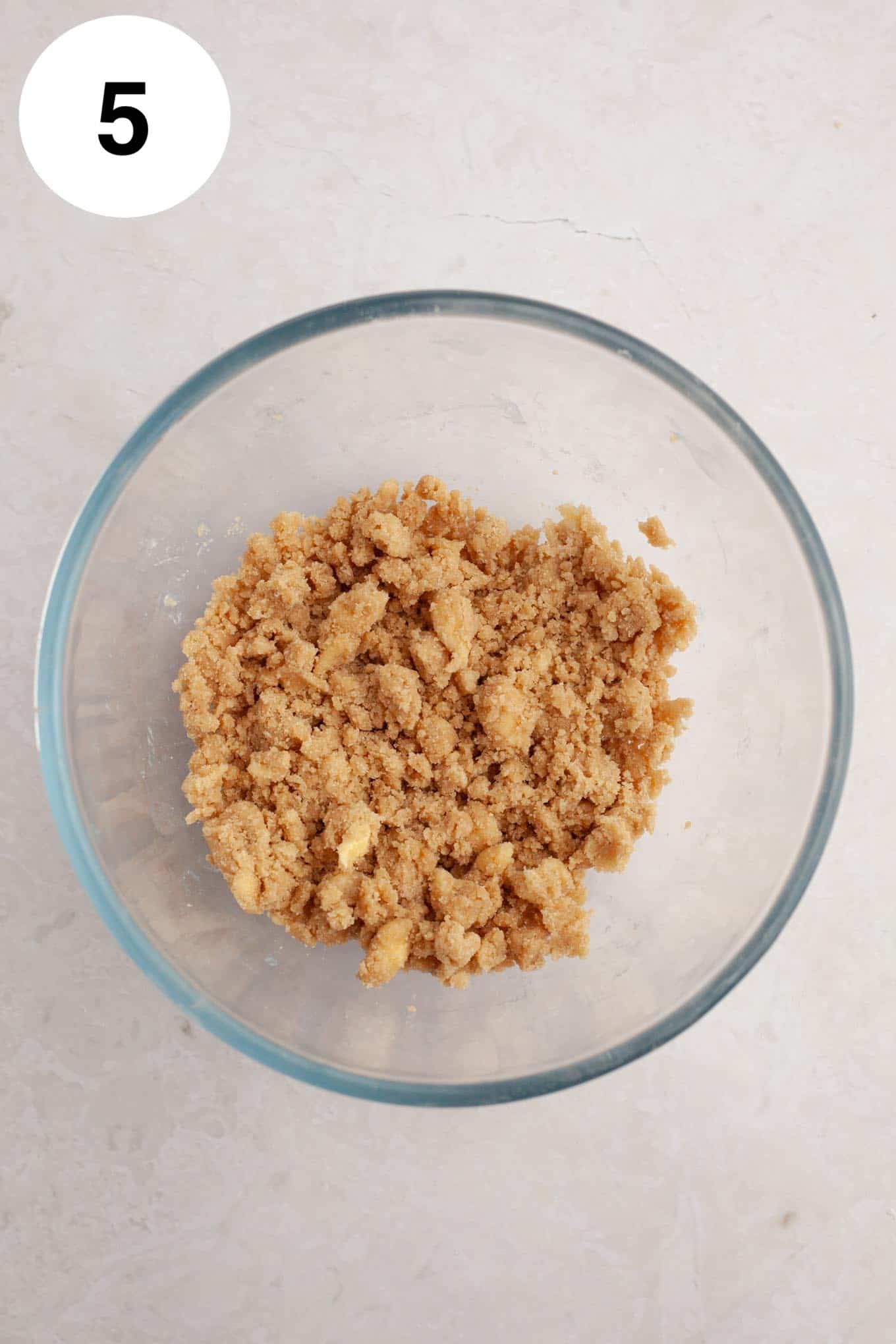 An overhead view of cinnamon streusel in a glass mixing bowl. 