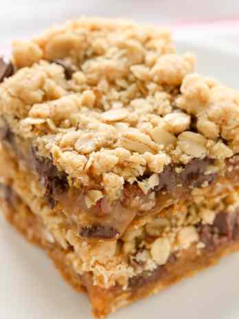 A stack of soft oatmeal crumb bars stuffed with gooey caramel, chocolate chips, and chopped pecans.