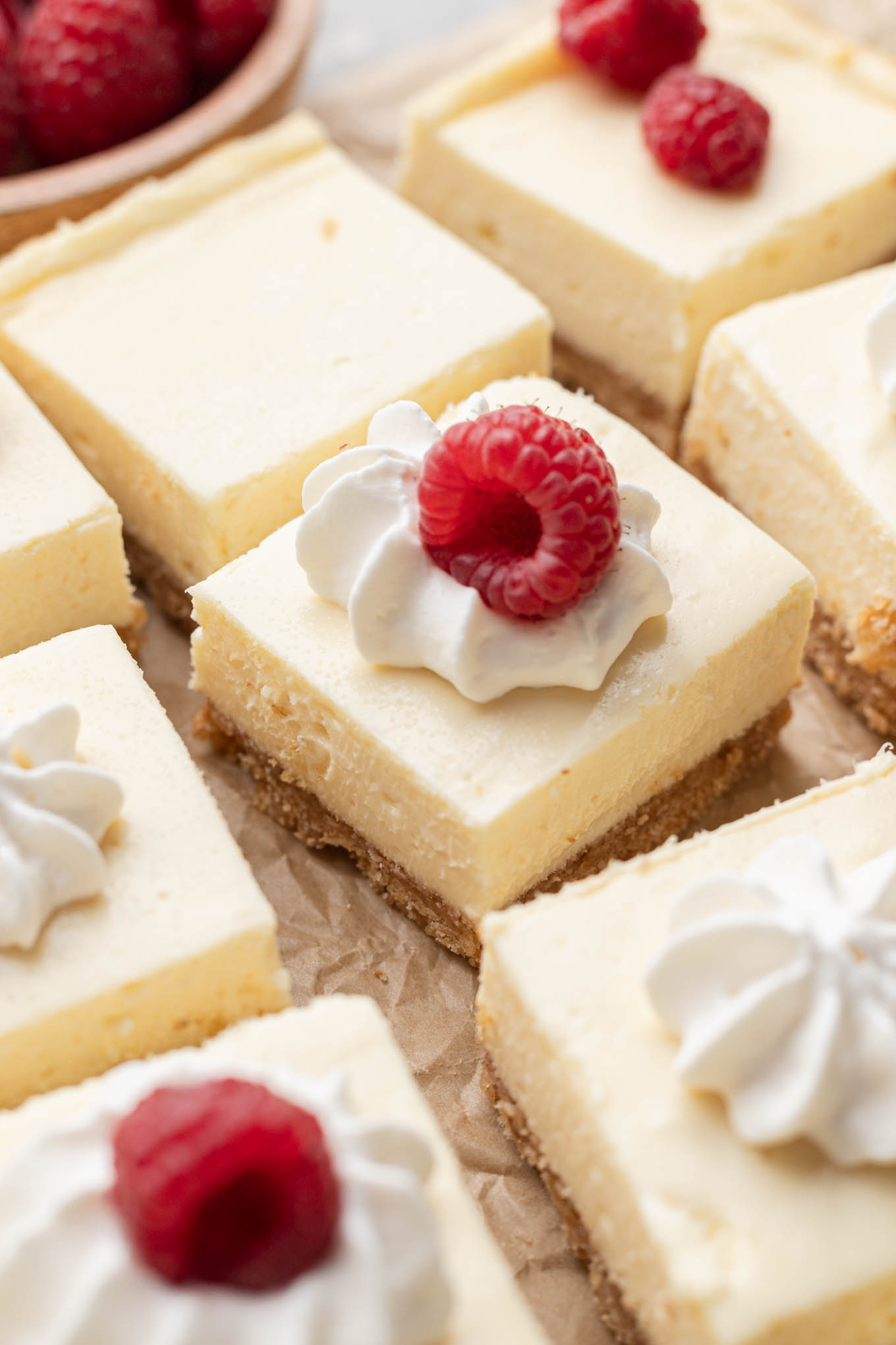 Sliced cheesecake bars topped with whipped cream and fresh raspberries.