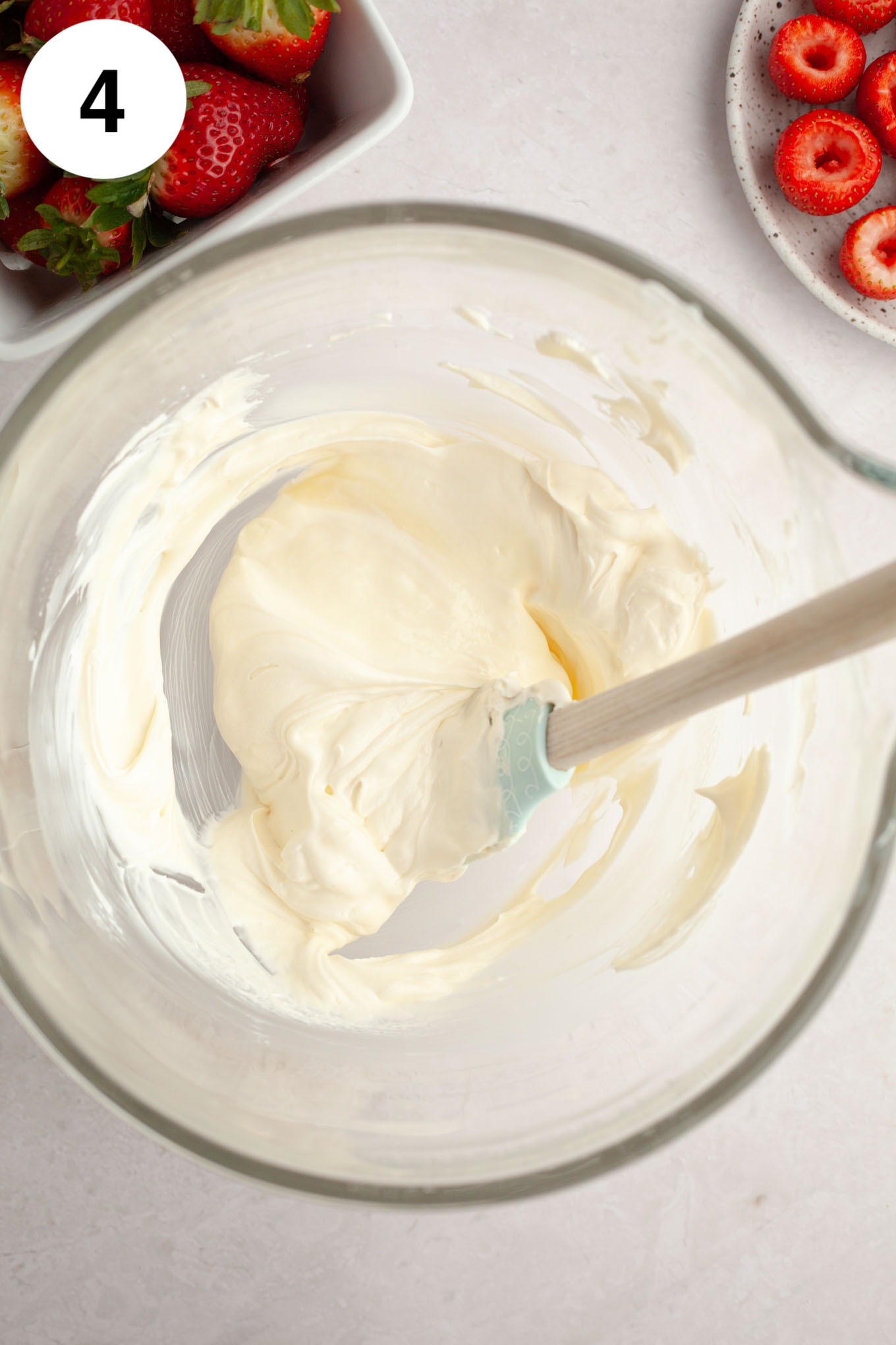 An overhead view of cheesecake filling in a glass mixing bowl with a rubber spatula.