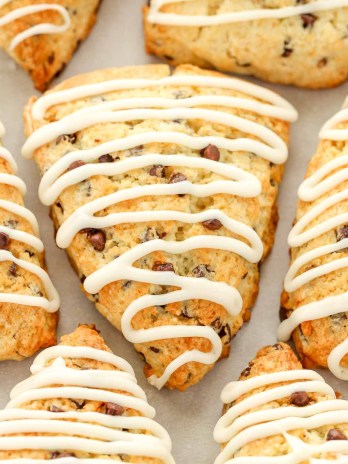 Several iced chocolate chip scones sitting on top of a piece of parchment paper.
