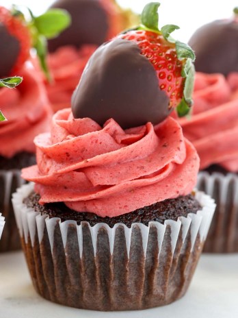 A closeup of chocolate cupcakes topped with strawberry buttercream frosting and chocolate covered strawberries.