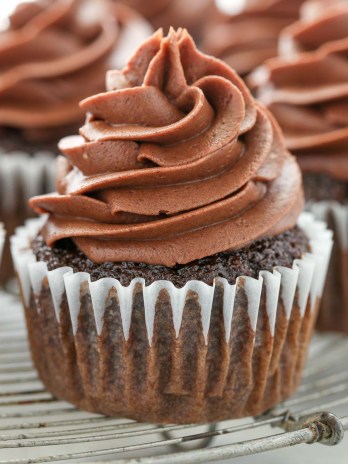 A close up picture of a chocolate cupcake topped with chocolate cream cheese frosting on an antique wire rack.