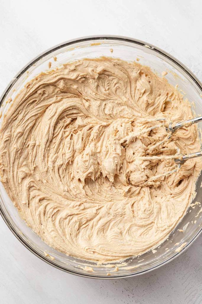 An overhead view of peanut butter buttercream frosting in a glass mixing bowl. 