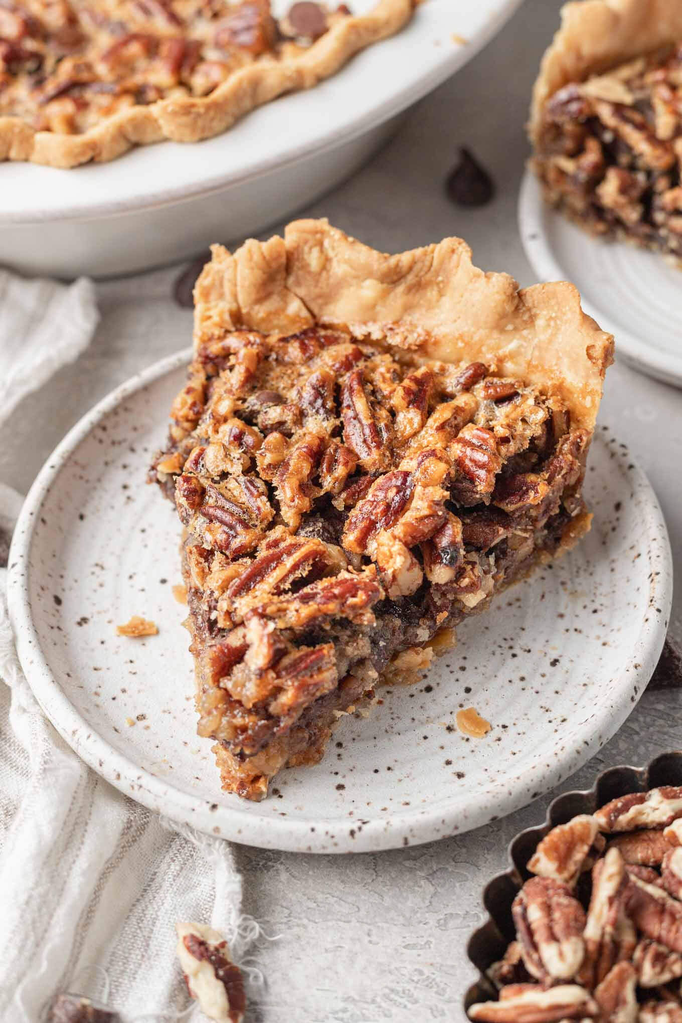 A slice of pecan pie with chocolate chips on a speckled dessert plate.