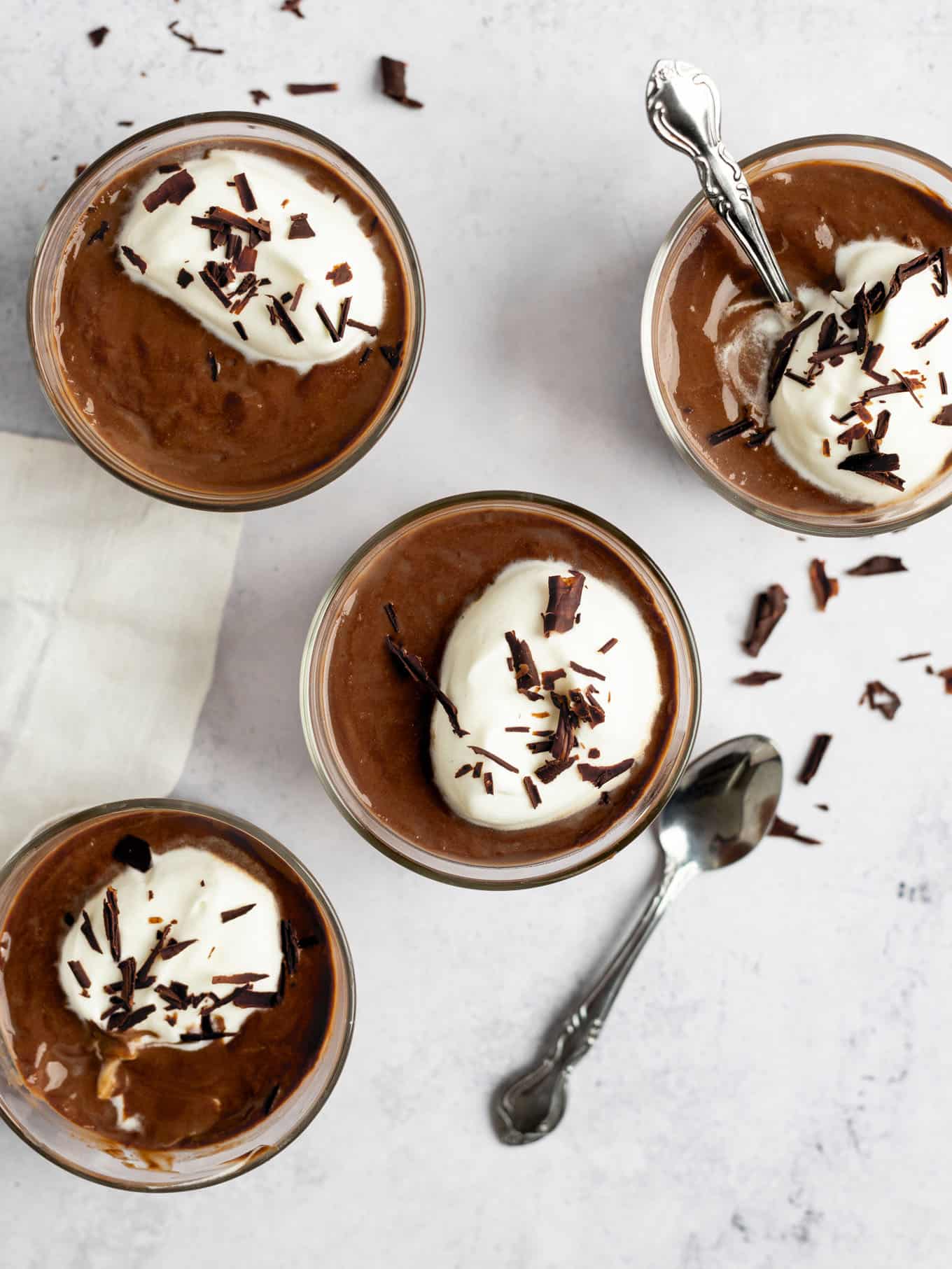 An overhead view of four pots of chocolate pudding garnished with whipped cream and chocolate shavings. 