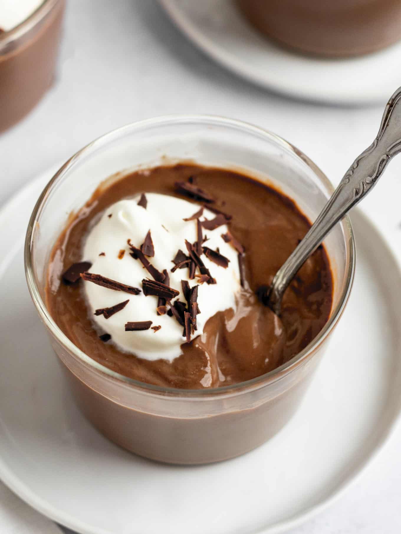 Homemade chocolate pudding garnished with whipped cream and chocolate shavings in a glass serving dish.