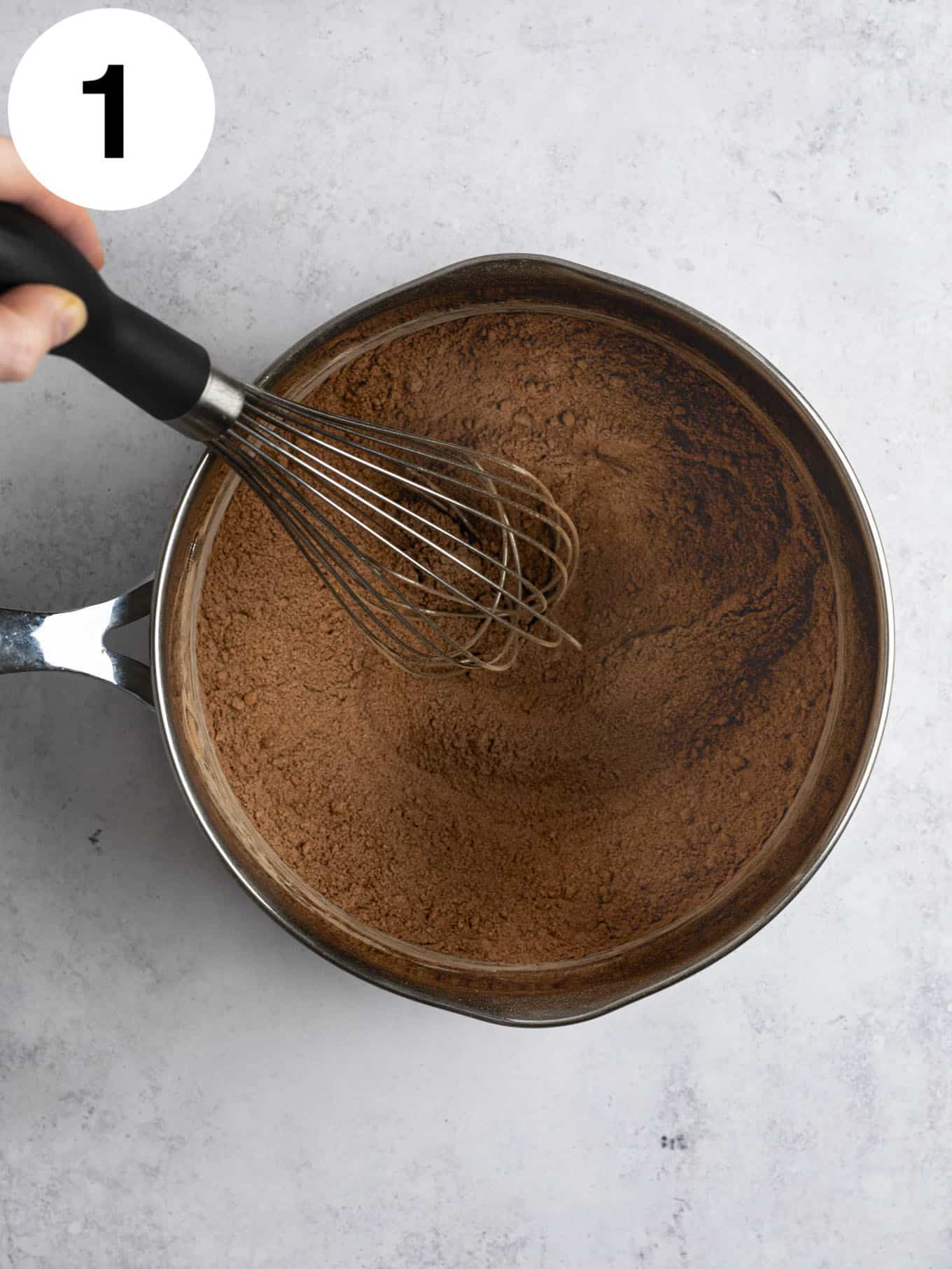 An overhead view of a cocoa powder mixture in a metal saucepan. 