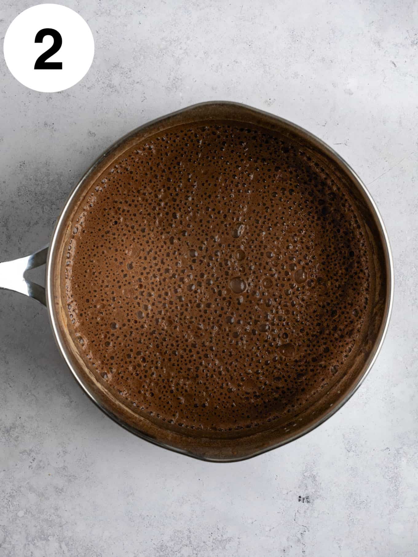 An overhead view of a milk and cocoa powder mixture in a metal saucepan. 
