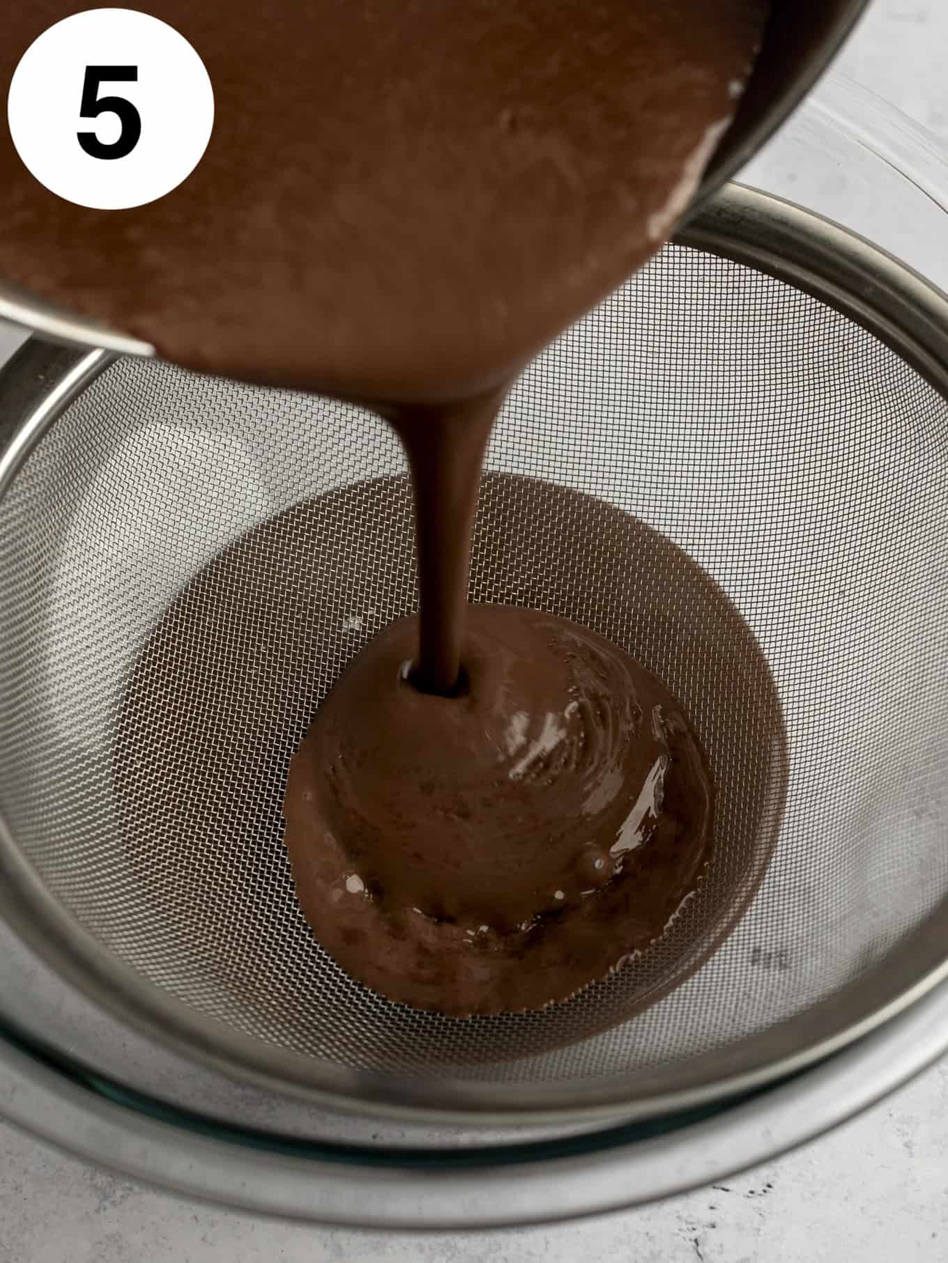 A process shot showing chocolate pudding being strained through a fine mesh sieve. 