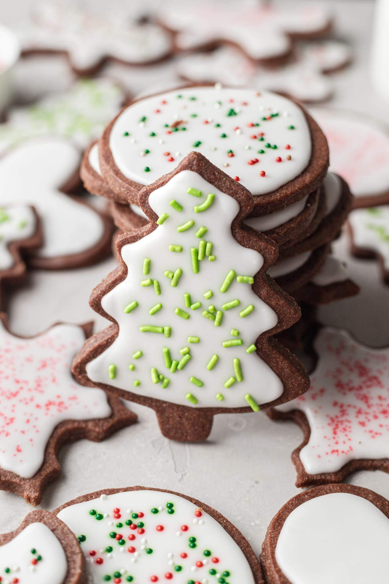 A stack of chocolate sugar cookies, decorated with icing and sprinkles. A tree-shaped cookie leans against the stack.