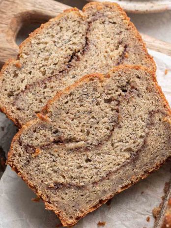 Two slices of cinnamon banana bread laying on a cutting board next to the rest of the loaf.