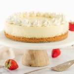 A cheesecake topped with whipped cream sitting on a marble cake stand.