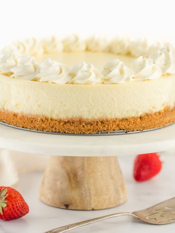 A cheesecake topped with whipped cream sitting on a marble cake stand.