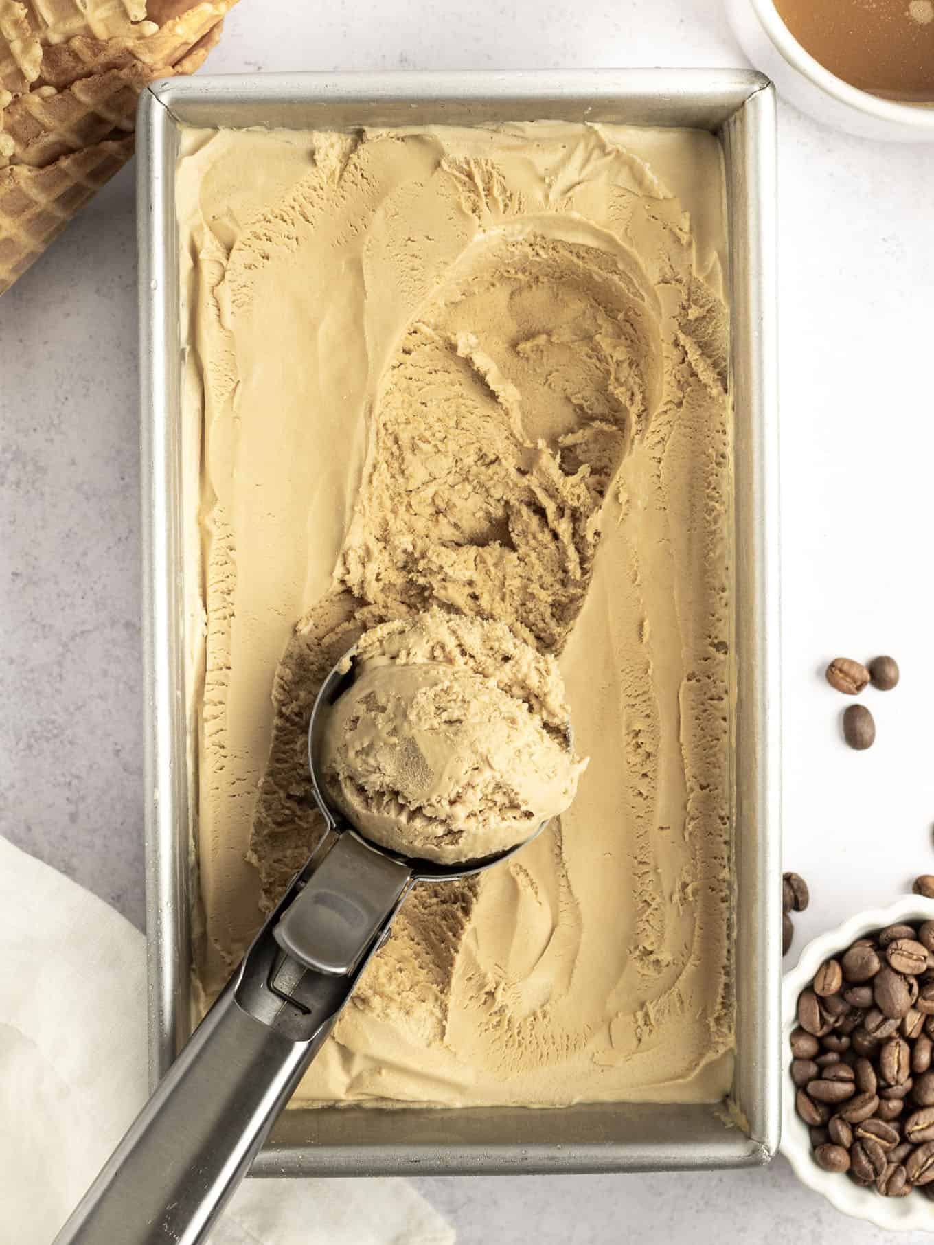 An overhead view of coffee flavored ice cream with an ice cream scoop resting on top of the loaf pan. 