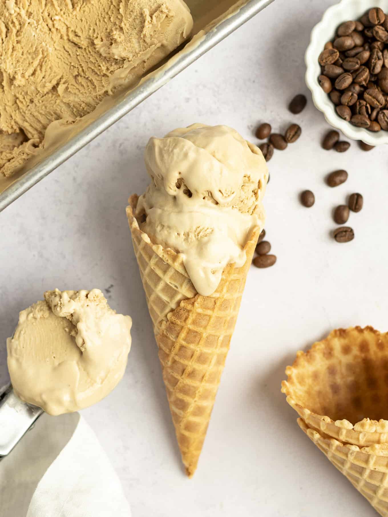 An overhead view of a coffee ice cream cone lying on its side, surrounded by coffee beans and additional cones. 