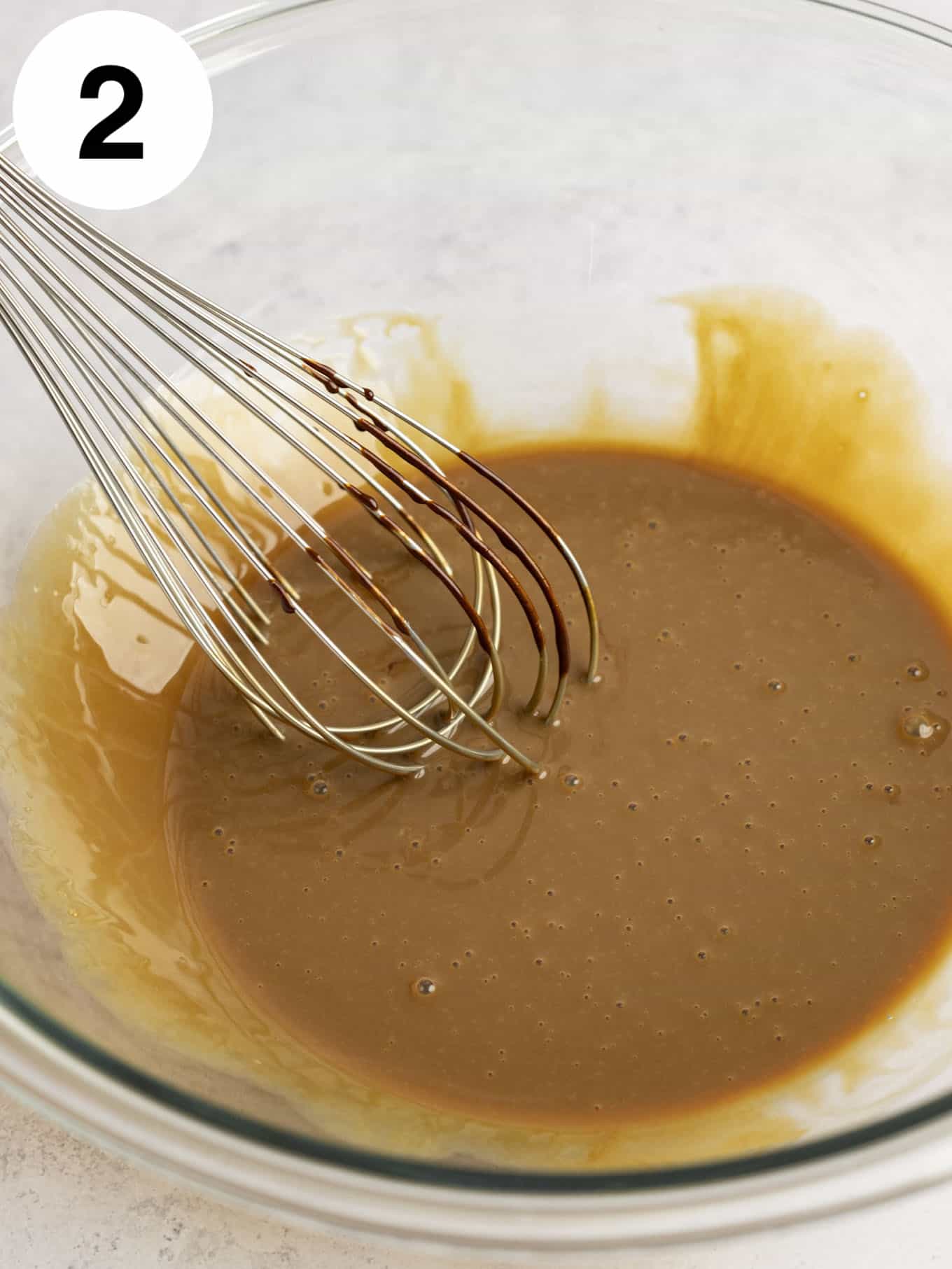 An overhead view of a coffee ice cream mixture in a glass bowl, with a whisk. 