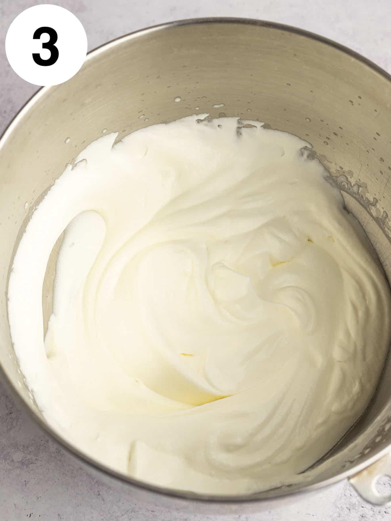 An overhead view of whipped cream in the bowl of a stand mixer. 