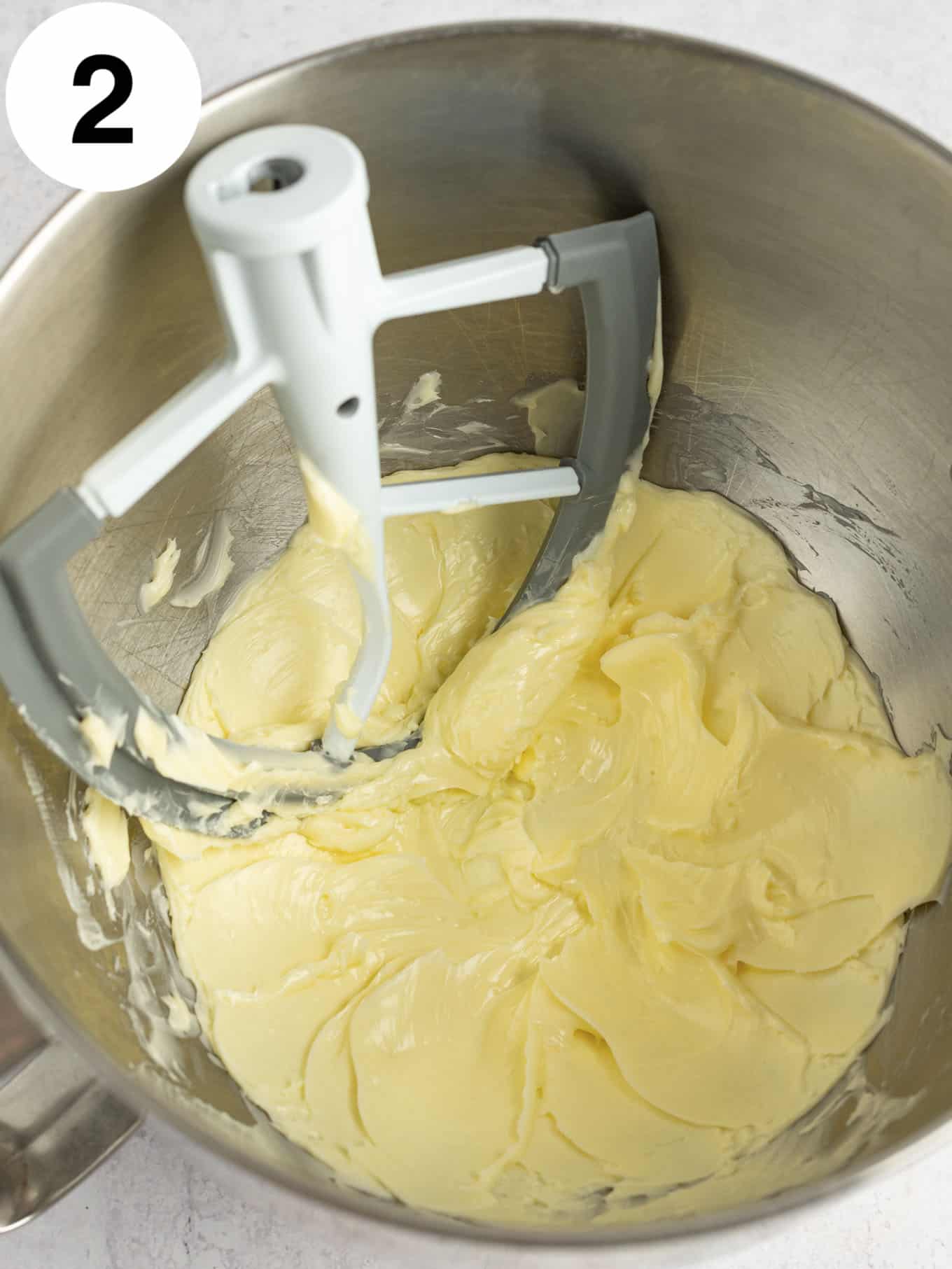 An overhead view of beaten butter in a stand mixer, with a paddle attachment. 