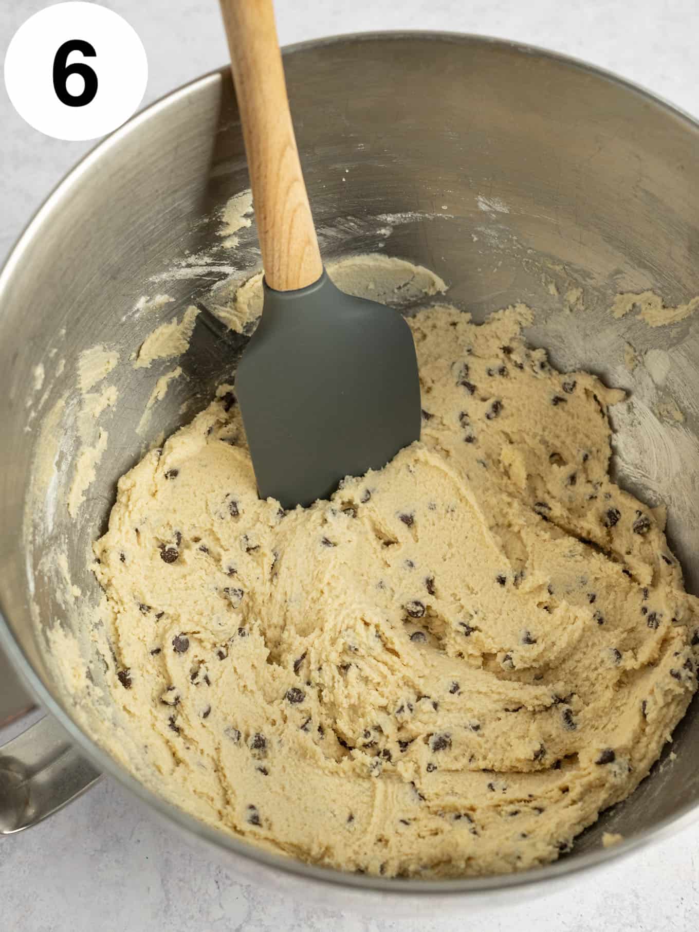 An overhead view of chocolate chip cookie dough frosting in the bowl of a stand mixer, with a paddle attachment. 