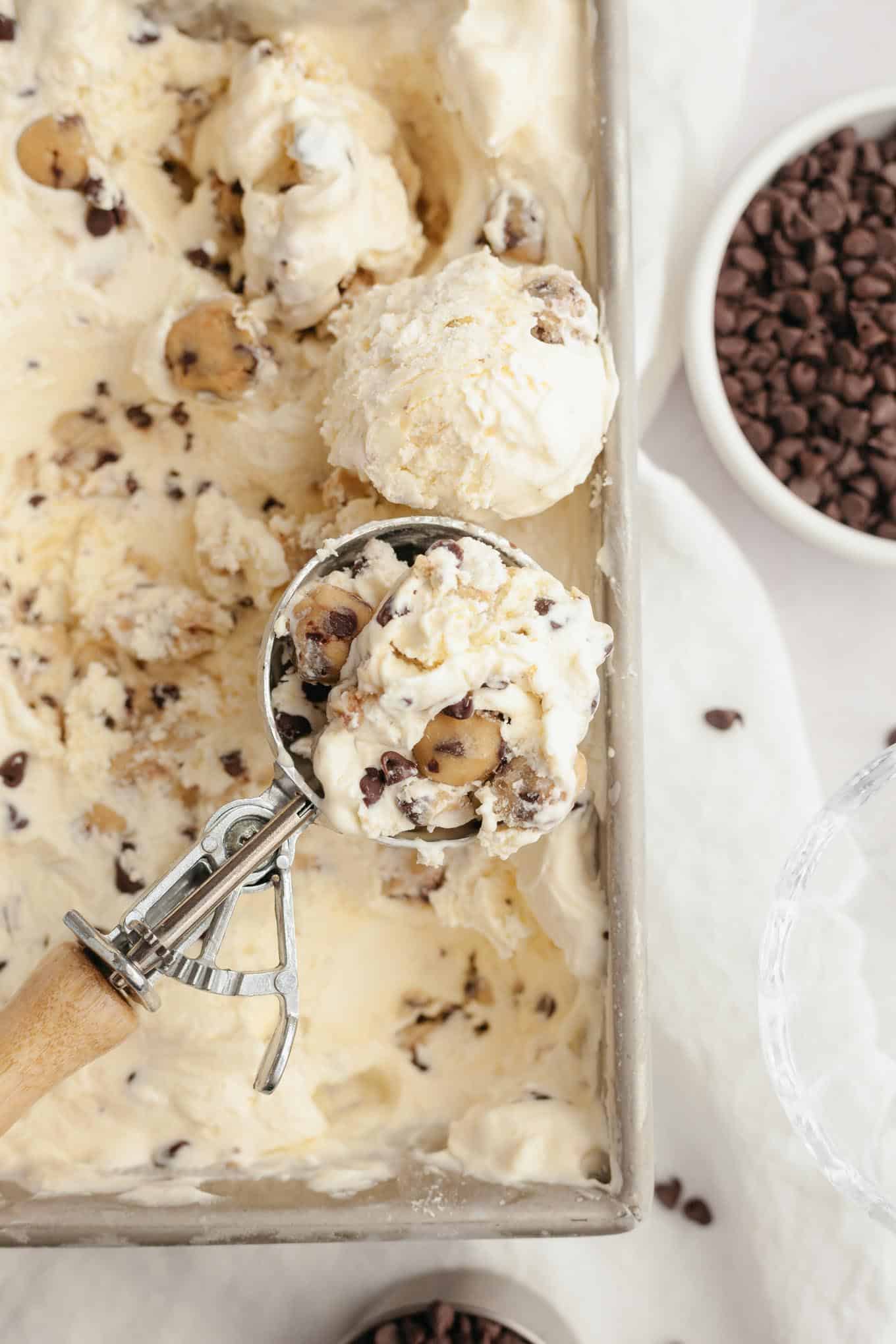 An overhead view of an ice cream scoop full of cookie dough ice cream, resting on a pan of ice cream.