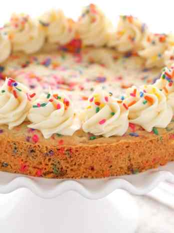 A sugar cookie cake topped with whirls of vanilla buttercream, seen from the side.