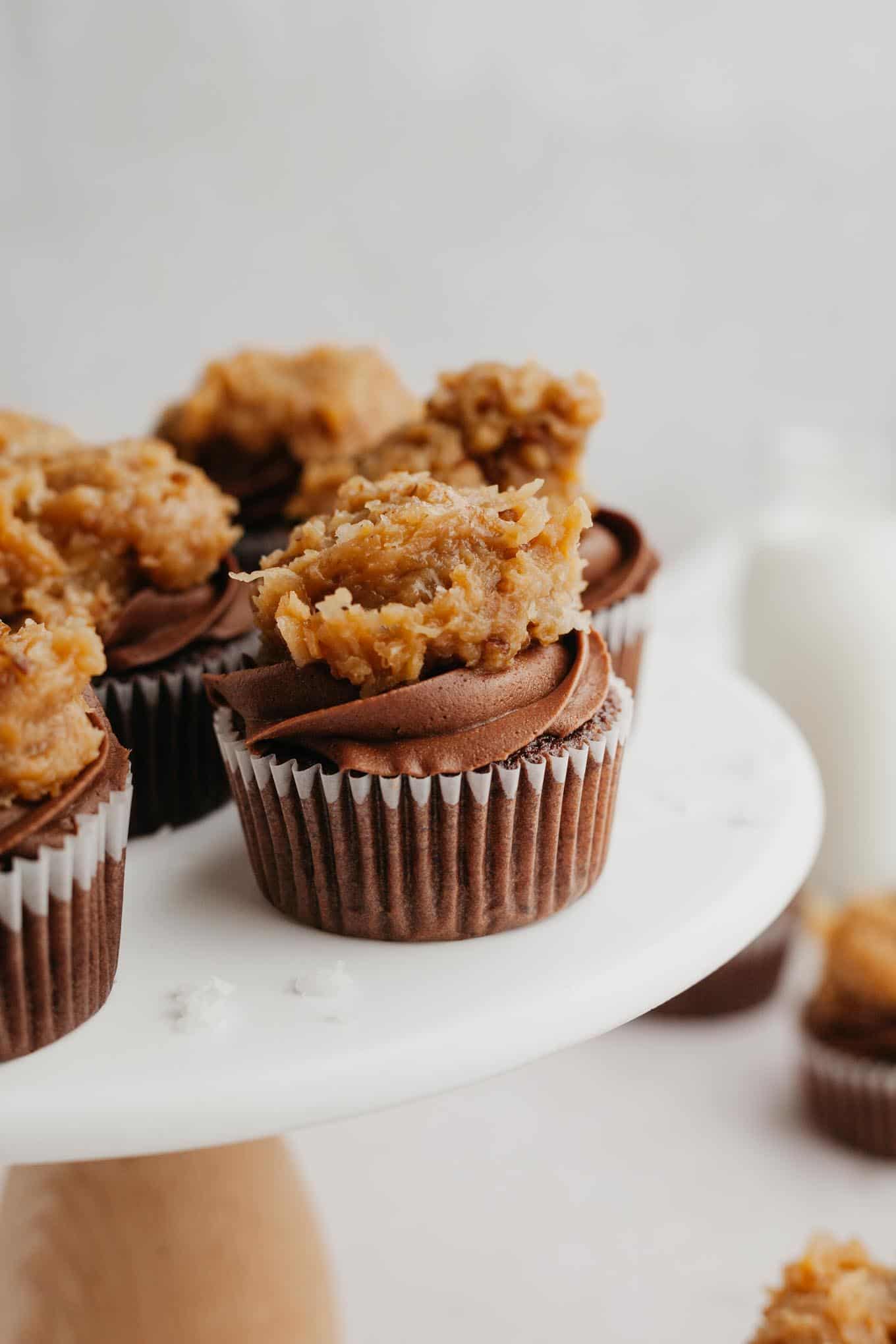 A side view of frosted German chocolate cupcakes on a marble cake stand. 