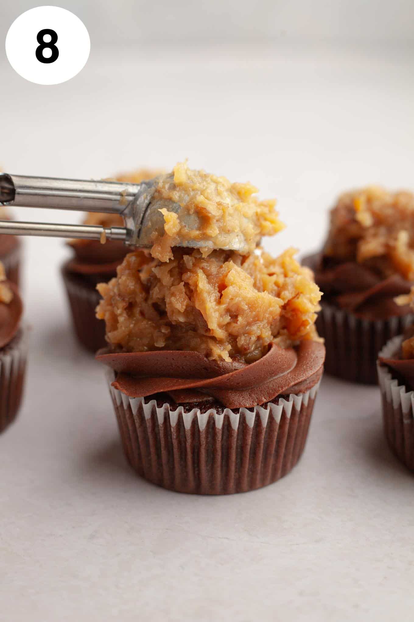 A process shot showing German chocolate frosting being dolloped onto chocolate cupcakes. 