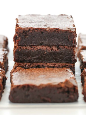 A stack of sliced brownies on parchment paper with more brownies around it.