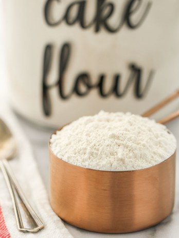 A close-up picture of a copper measuring cup filled with cake flour.
