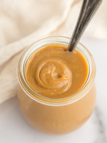 A close-up image of dulce de leche in a small glass jar.