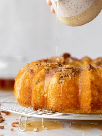 A baked rum cake resting on a round cooling rack and the rum glaze being poured over the top.
