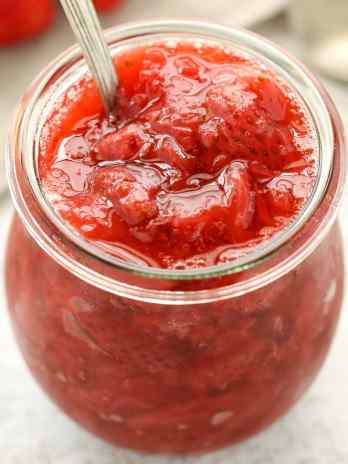 Homemade strawberry sauce in a glass jar with a spoon sticking out.