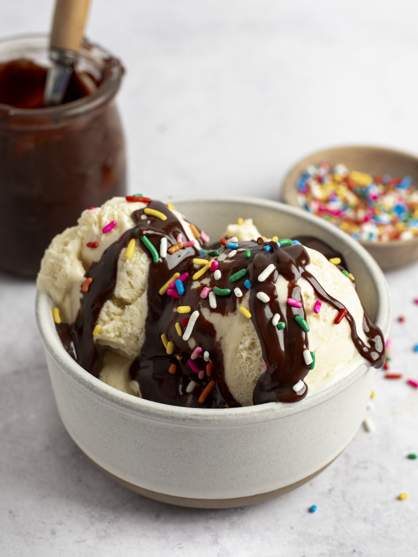 A dish of ice cream topped with hot fudge and rainbow sprinkles.