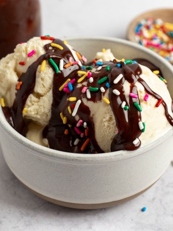 A bowl of ice cream topped with hot fudge sauce and sprinkles.