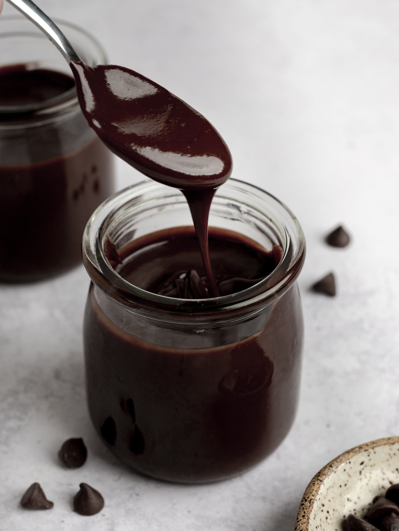 A spoonful of hot fudge sauce being held over a glass jar. 
