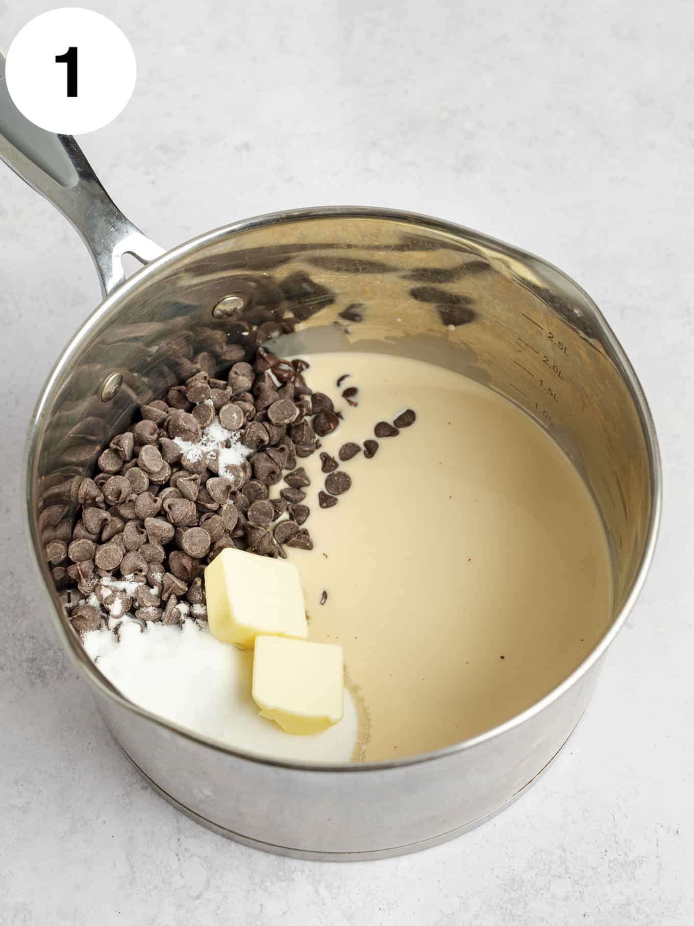 A metal saucepan full of evaporated milk, sugar, butter, salt, and chocolate chips. 