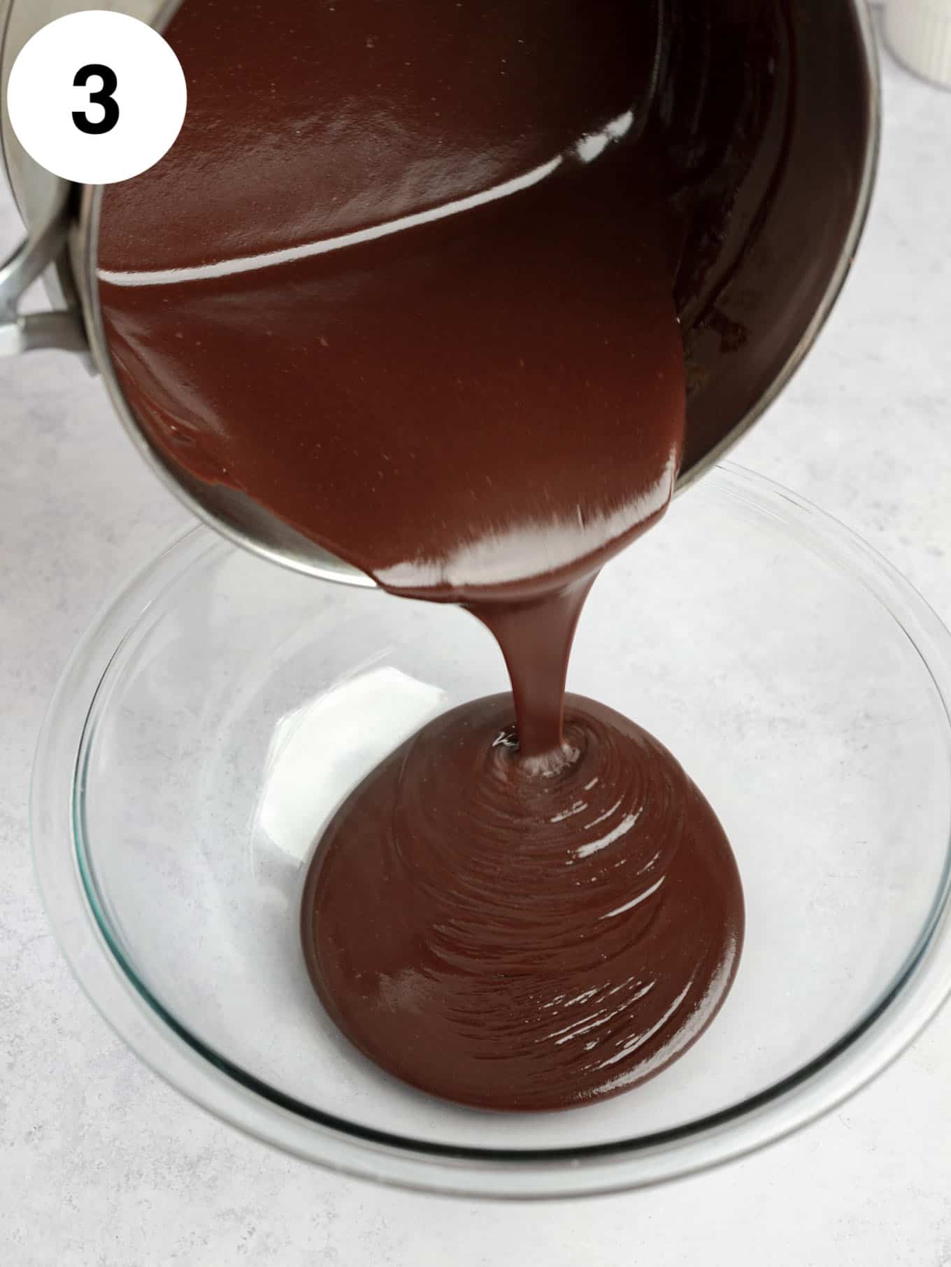 An action shot showing hot fudge sauce being poured into a glass bowl. 