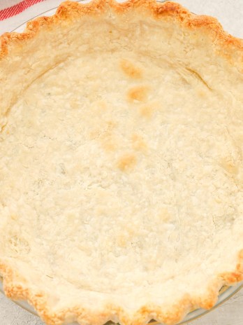 Overhead view of a blind baked pie crust next to a striped towel.