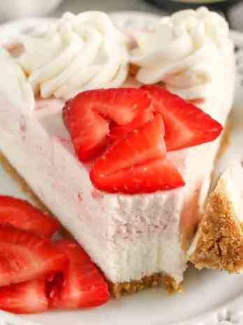 A slice of no bake strawberry cheesecake on a white dessert plate with berry slices and a fork.