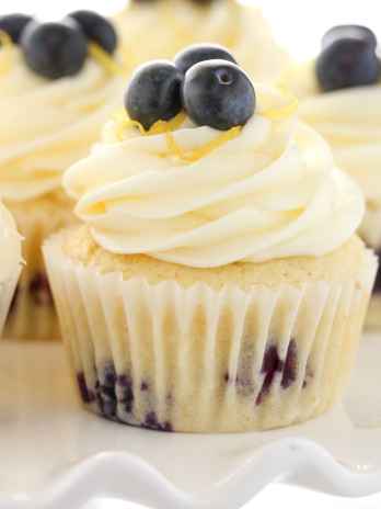Side view of lemon blueberry cupcakes topped with lemon frosting on a white cake stand.