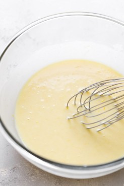 Wet ingredients and a whisk needed to make muffins in a glass mixing bowl.